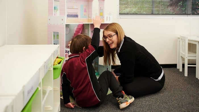 Boy and therapist play with dolls house