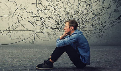 A young man sits on the floor holding his knees and looks overwhelmed.