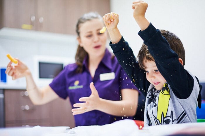 A young boy crumbling a cracker with a therapist cheering him on