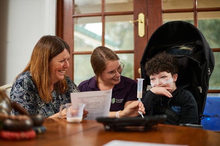 A parent and therapist smiling at a child being tube fed