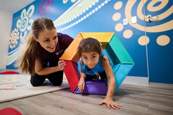 A therapist watching a child crawl through a play tunnel