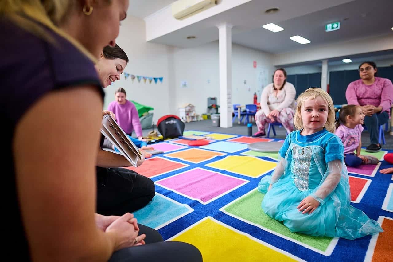 Therapists, parents and kids sitting and playing on colourful mat