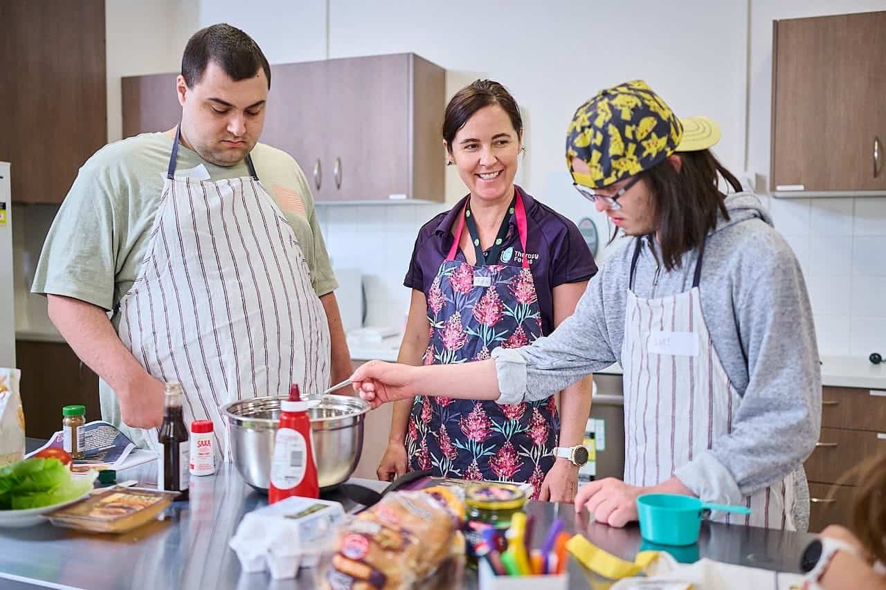 A dietitian supports two young men during a group cooking class